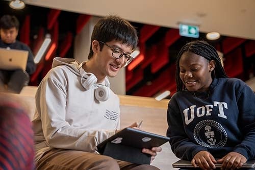 Two UUֱ students smiling and looking at a tablet